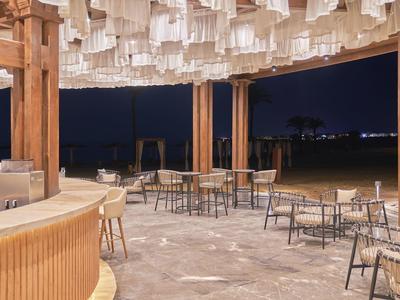 Offener Restaurantbereich mit Holzsäulen, Tischen, Stühlen und Decke mit weißen Lampenschirmen bei Nacht.