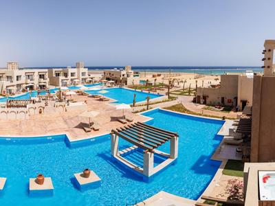Großer Hotelpool mit blauen Wasserflächen, Liegestühlen und Blick auf das Meer