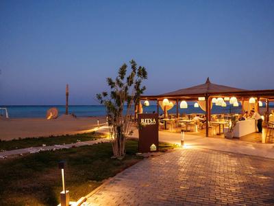 Bar de playa por la noche con camino iluminado y amplia vista al mar bajo un cielo azul.