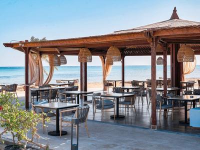 Offenes Strandrestaurant mit Holzdach und Tischen mit Blick auf das Meer.
