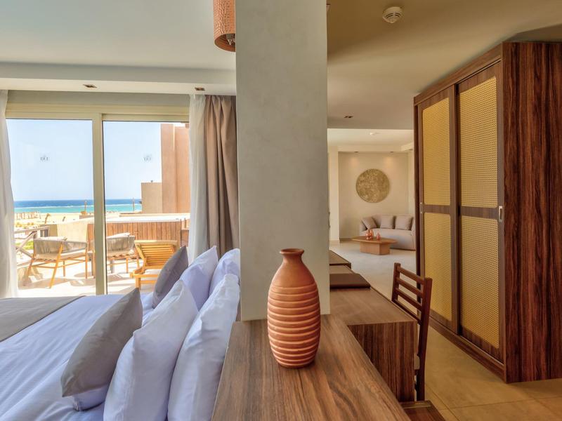 Camera d'hotel moderna con letto, mobili in legno e balcone con vista mare.