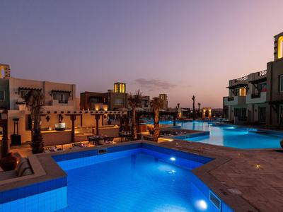 Complexe hôtelier moderne avec piscine éclairée au coucher du soleil aux tons chauds.