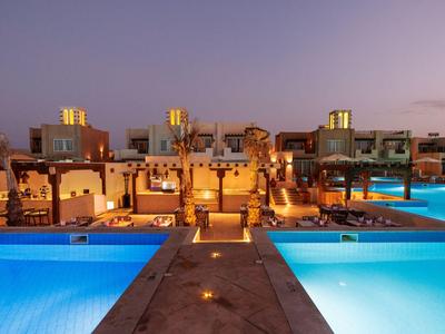 Modern hotel complex with illuminated pool at sunset.