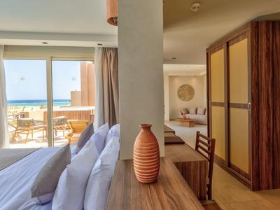 Helles Schlafzimmer mit Bett, Holzschrank, Terrassentüren und Blick auf das Meer.