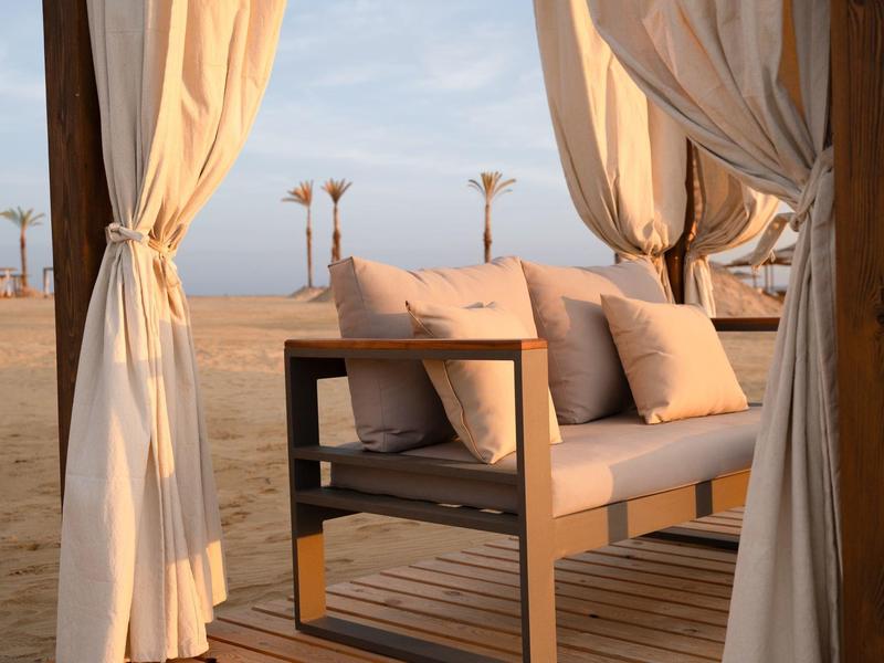 Gemütliche Lounge mit Holzsofa und Kissen, umgeben von weißen Vorhängen in Wüstenumgebung.