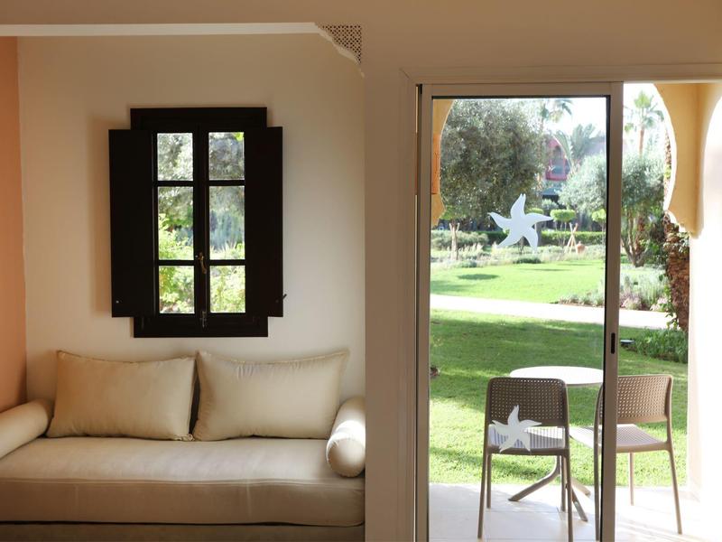 Pohodlná pohovka vedle otevřených dveří s výhledem na zahradu se židlemi.