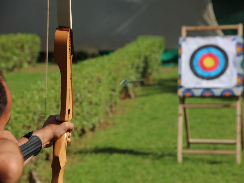 Osoba cvičící lukostřelbu venku s terčem na zelené trávě