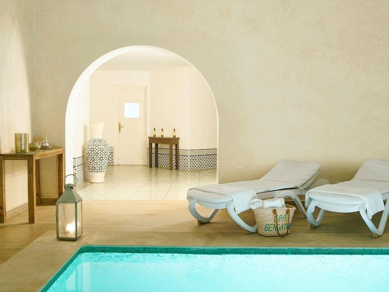 Obývací prostor s bazénem, dvěma bílými lehátky a dekorativními prvky v světlé místnosti.