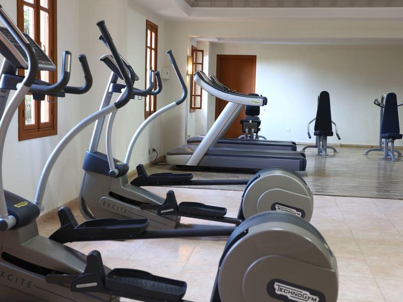 Fitness místnost s eliptickými trenažéry a běžeckými pásy před velkým zrcadlem.