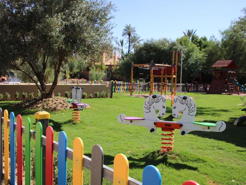 Barevné dětské hřiště s houpačkou a prolézačkou na zelené trávě za slunečného počasí