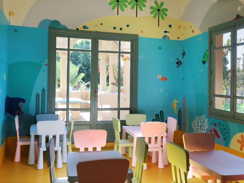 Barevná dětská herna s malými stoly, židlemi a zdí zdobenou podmořskými malbami.