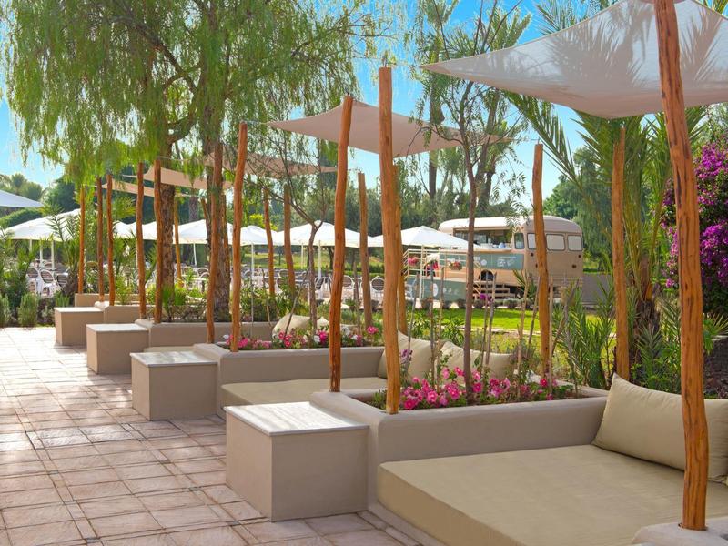 Moderní venkovní prostor s posezením, rostlinami a slunečníky v hotelové zahradě.