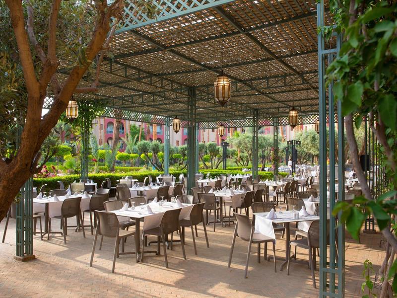 Zastřešená venkovní terasa s prostřenými stolky a židlemi v hotelové zahradě.