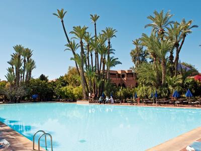 A large pool surrounded by palm trees and lounge chairs in front of a hotel building.