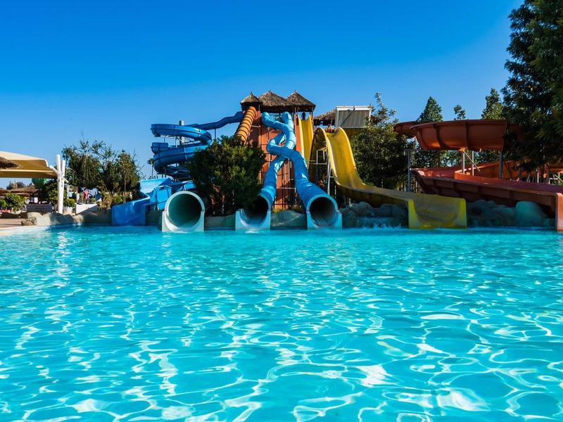 Grand bassin extérieur avec toboggans aquatiques et eau bleue claire sous un ciel dégagé.