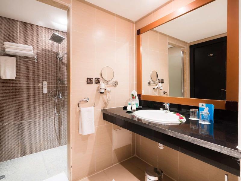 Salle de bain d'hôtel lumineuse avec douche en verre, grands miroirs et plans noirs.