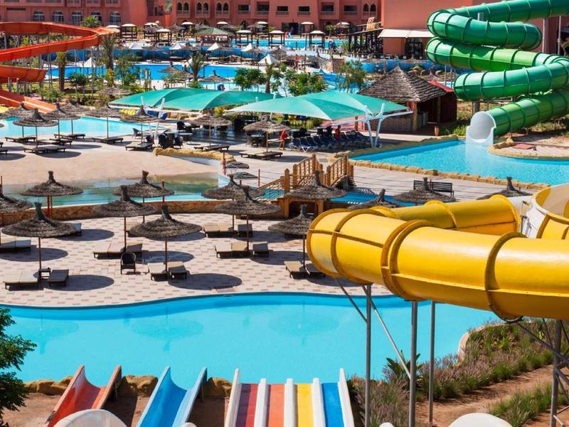 Parc aquatique coloré avec toboggans, piscines et chaises longues devant les montagnes.