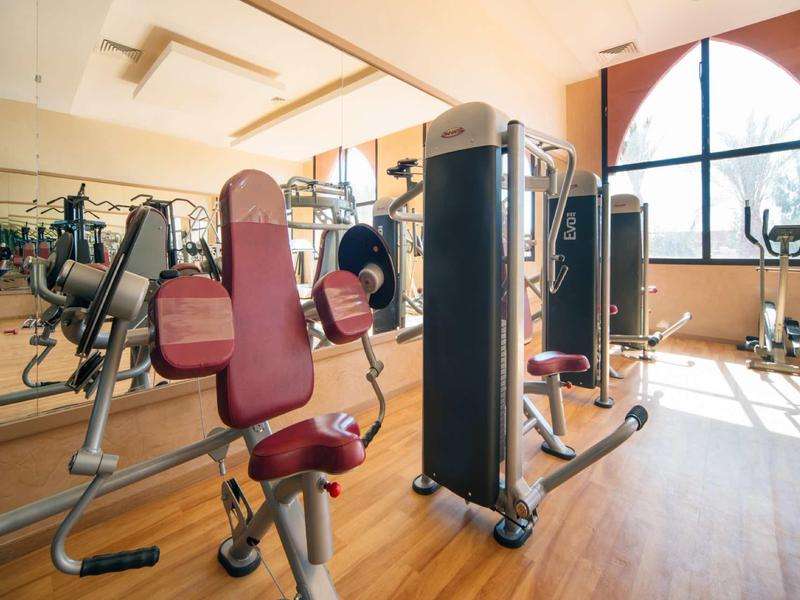 Salle de sport lumineuse avec équipements modernes et sol en bois, lumière traversant une grande fenêtre.