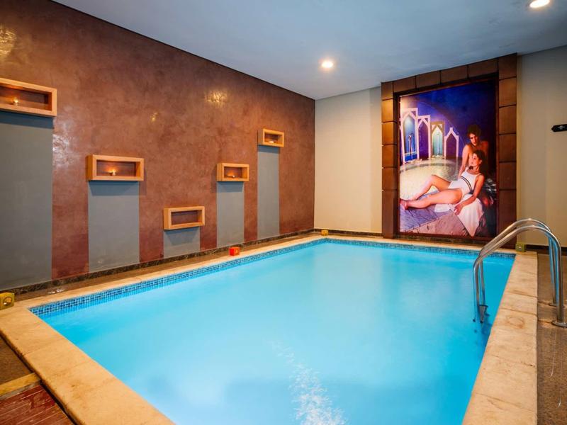 Piscine intérieure avec eau claire, éclairage chaud et fresque murale décorative dans un hôtel.