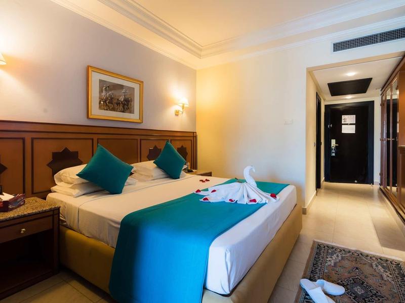 Chambre d'hôtel confortable avec lit double, coussins bleus et décoration en forme de cygne sur la couverture.