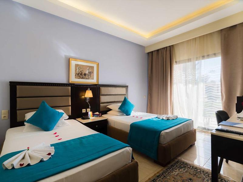 Chambre d'hôtel avec deux lits simples, oreillers bleus, serviettes décoratives et bureau près de la fenêtre.