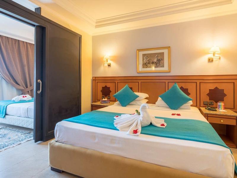 Lit double confortable avec accents turquoise dans une chambre d'hôtel lumineuse avec balcon attenant.