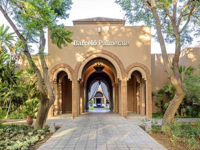 Eingang zu einem Hotel mit bogenförmiger Architektur und Spazierweg, umgeben von Bäumen.