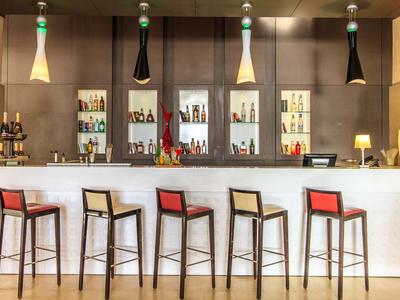 Moderní hotelový bar s pěti barovými židličkami a osvětlenou expozicí nápojů v pozadí.