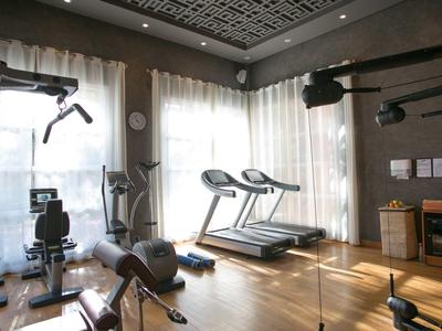 Helles Fitnessstudio mit Laufbändern, Trainingsgeräten und großen Fenstern mit Vorhängen.