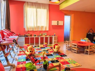 Barevná dětská herna s kobercem, hračkami, židlemi a stoly v teplém osvětlení