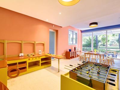 Světla herna s fotbálkem, dětskými stoly, židlemi a velkým oknem s výhledem na zahradu.