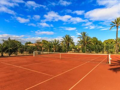 Roter Tennisplatz mit Netzen, umgeben von Palmen und blauem Himmel mit Wolken.