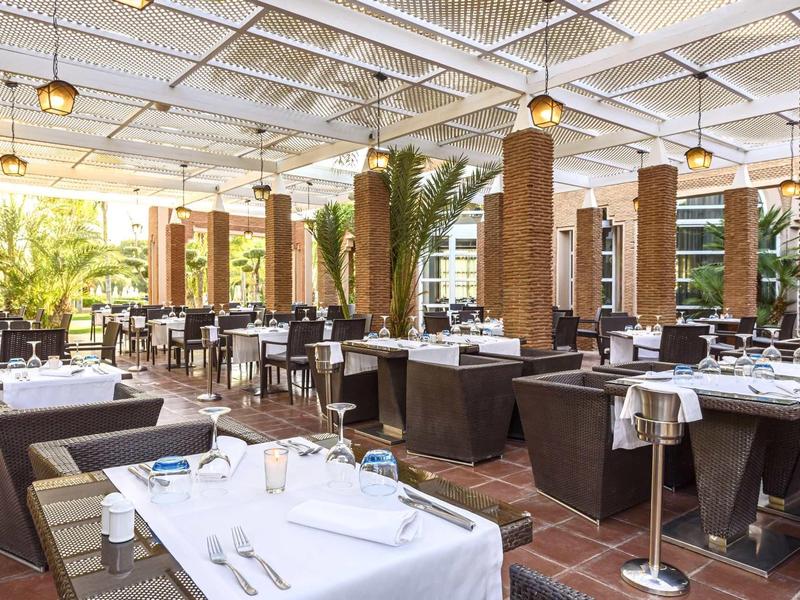 Elegantní restaurace s bílými ubrusy a dřevěným nábytkem v prosvětlené místnosti s velkými okny.