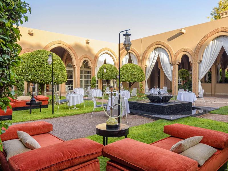 Nádvoří s červeným posezením, zelenými stromy a žlutými obloukovými zdmi.