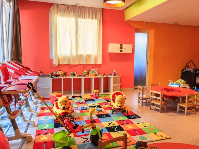 Barevná dětská herna s kobercem, hračkami, židlemi a stoly v teplém osvětlení