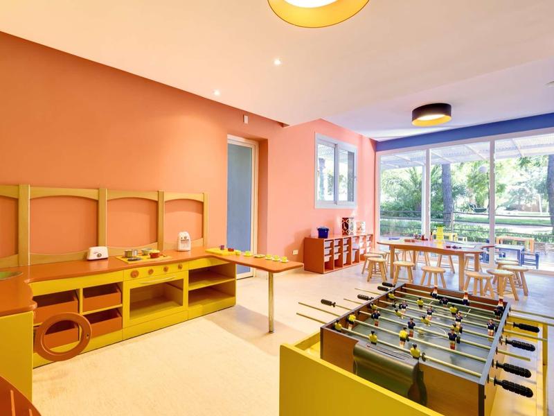 Světla herna s fotbálkem, dětskými stoly, židlemi a velkým oknem s výhledem na zahradu.