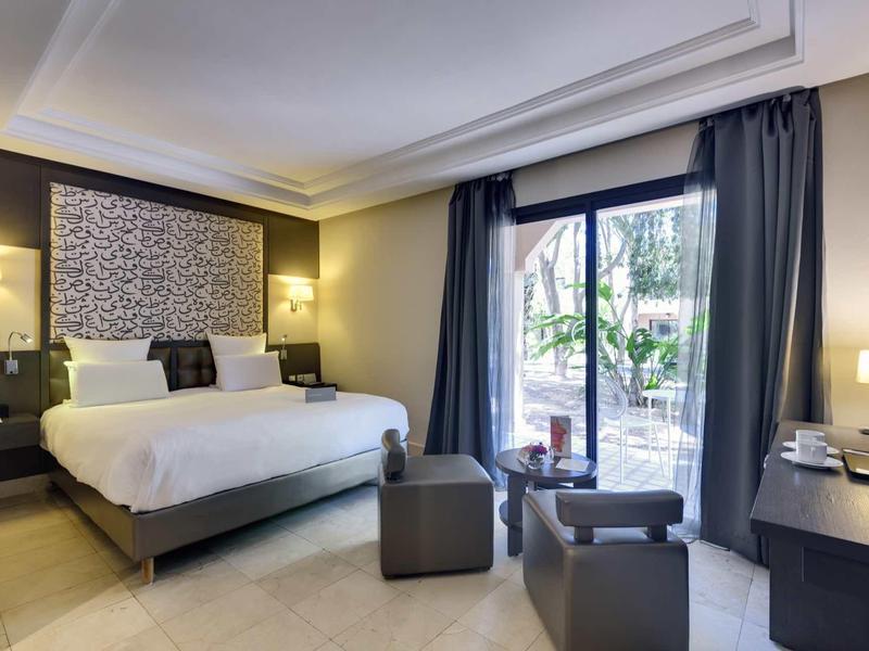 Moderní hotelový pokoj s velkou postelí, posezením a výhledem na terasu přes velká okna