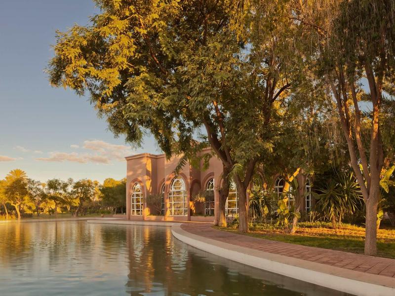 Večerní scéna s historickou budovou a jezerem obklopeným stromy.