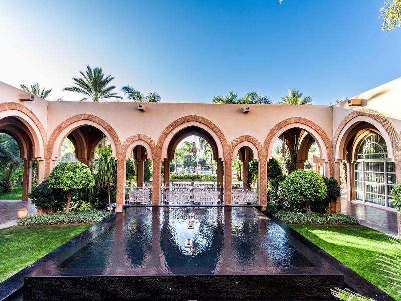 Nádvoří s růžovými oblouky, odrazovou vodou a zelení pod jasnou oblohou