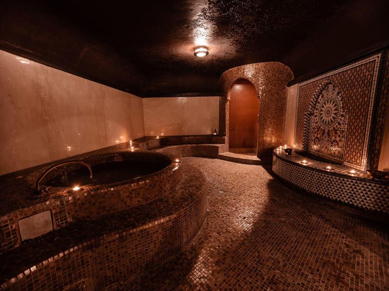 Sala spa di lusso con illuminazione calda, piastrelle a mosaico e vasca da bagno rotonda