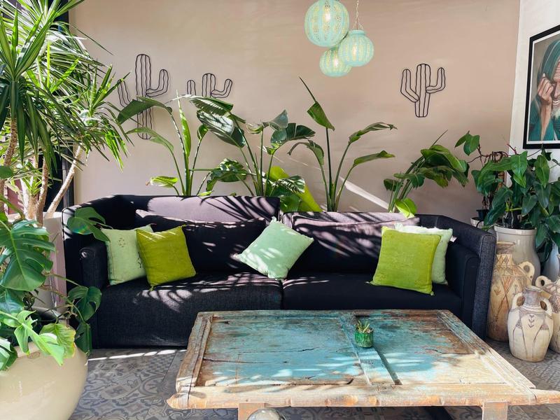 Soggiorno con divano blu scuro, cuscini verdi, tavolo rustico in legno e molte piante.