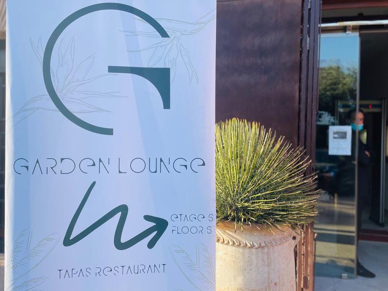 Ingresso della Garden Lounge con insegna e pianta accanto alla porta di vetro.