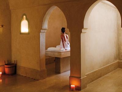 Woman sitting in a warmly lit spa area with candles and stone arches.