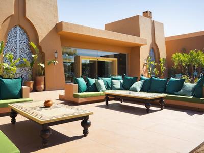 Gemütliche Terrasse mit niedrigen Sofas und blauen Kissen vor einem Gebäude mit großen Fenstern.