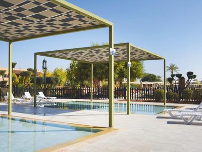Hotel pool area with sunshades and lounge chairs under clear sky.