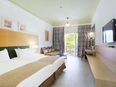 Bright hotel room with two beds, balcony, and modern wall-mounted TV.