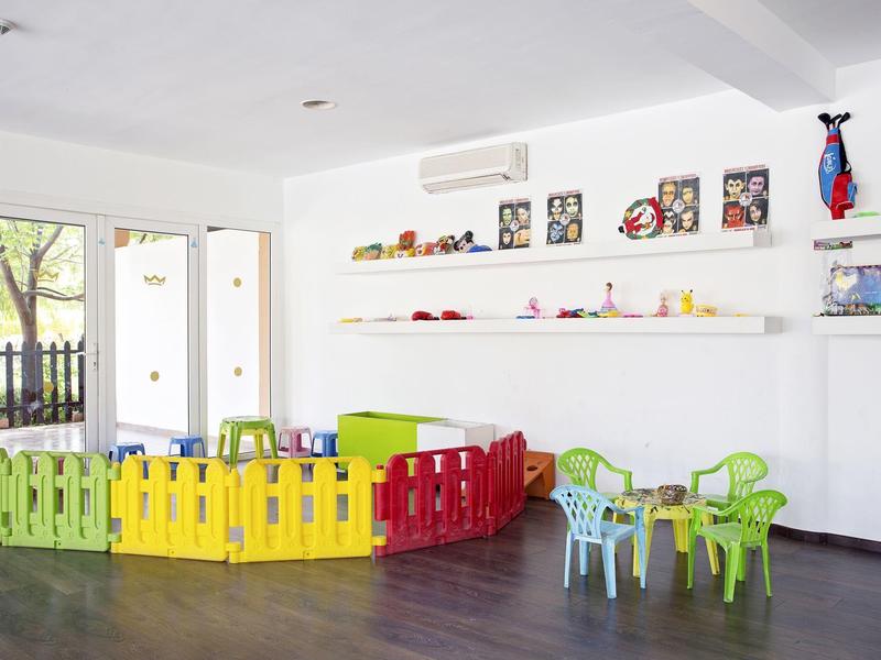 Children's play area with colorful fence and chairs in a bright room with large windows.