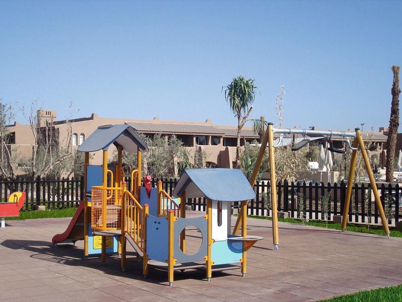 Colorful playground with slides and swings next to a hotel and fence.