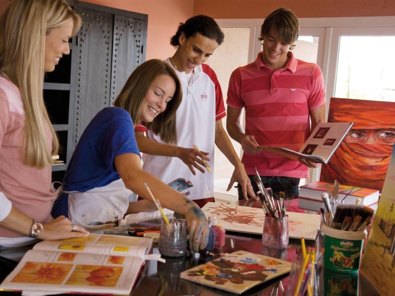 Four people painting together at a table full of art supplies in a bright room.