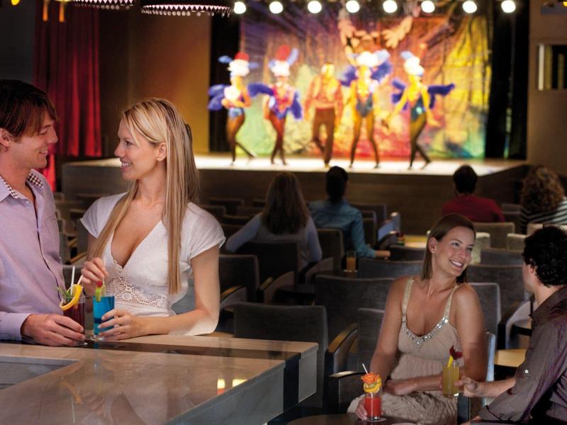 Guests enjoy cocktails at a bar with a colorful stage show in the background.